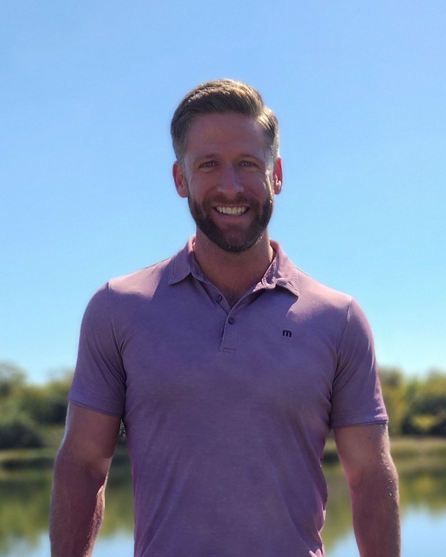 Nate Richard, standing outdoors in front of a lake on a sunny day.